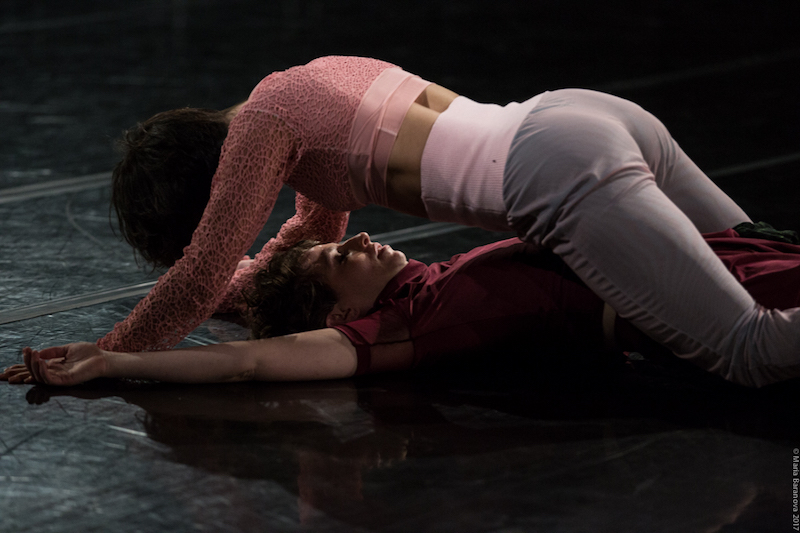 Molly Lieber in a pink crop top and grey pants hovers over Eleanor Smith who lays on the floor in a magenta top and pants 
